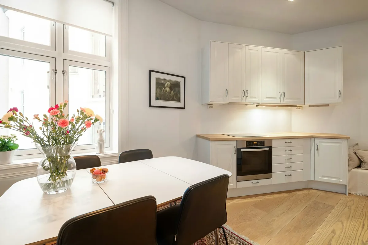 Eettafel bij het raam in een lichte woonkeuken met witte kastjes en een houten werkblad