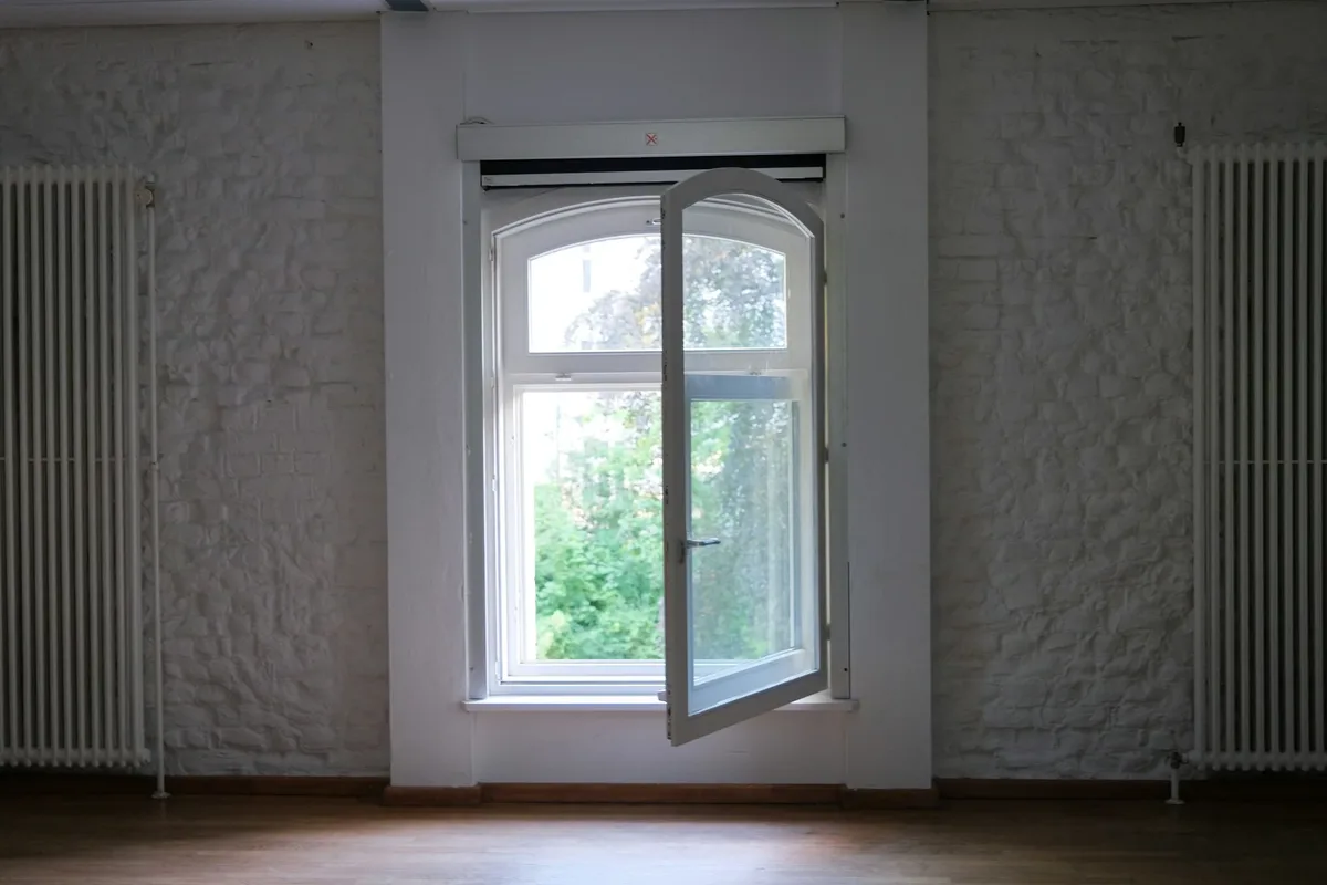 Lege kamer in een oud pand met witgeschilderde bakstenen wanden, twee radiatoren en een openstaand raam